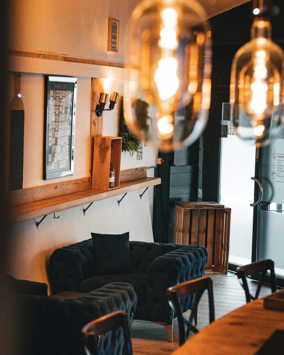 Salle d'Œno Bar à Pau : bar en bois noyer, bouteilles rétroéclairées et fauteuils en velours bleu nuit